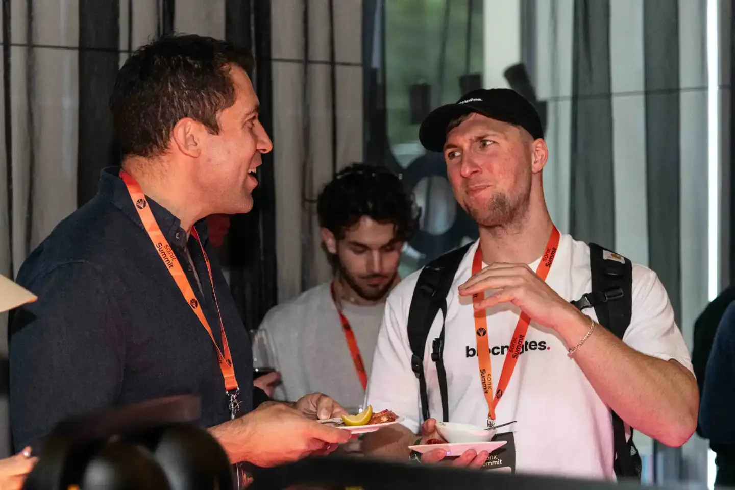 Zwei Männer mit Event-Lanyards unterhalten sich auf dem Sonic Summit in Wien, einer trägt ein weißes Shirt mit Logo