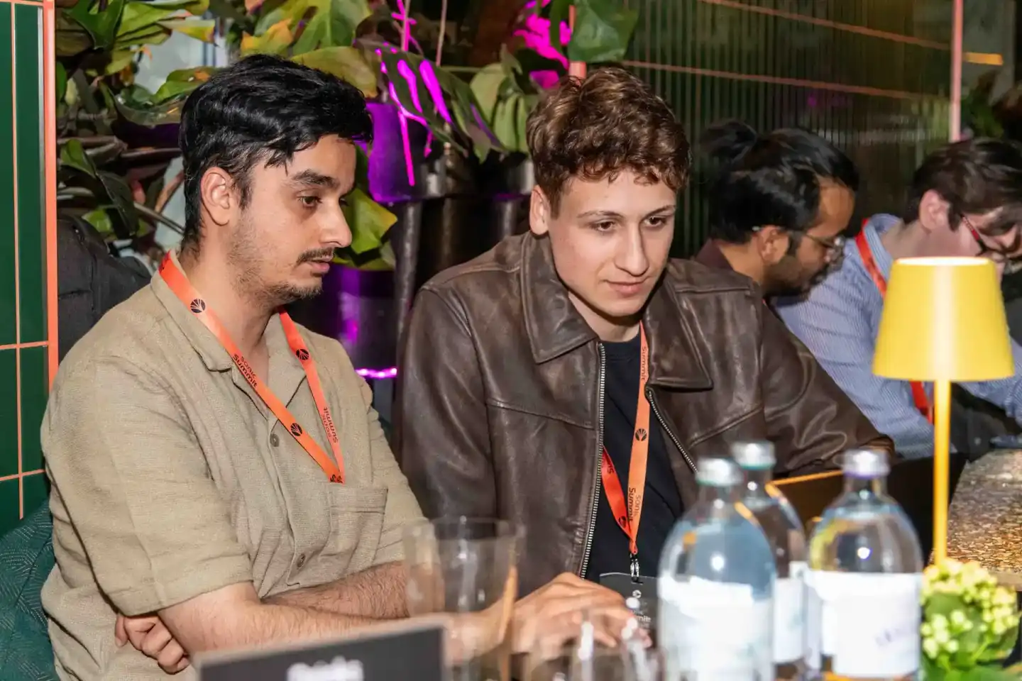 Zwei Männer mit Lanyards während des Sonic Summit Events in Wien, sitzend an einem Tisch mit Getränken und modernem Ambiente