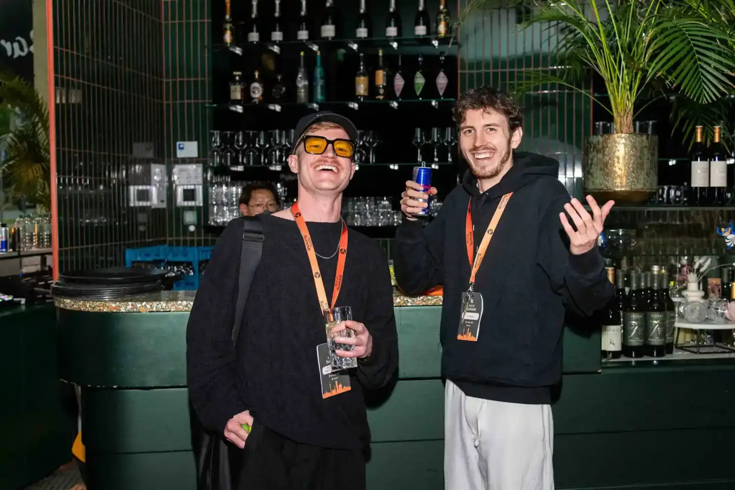 Zwei Männer mit Lanyards feiern an einer modernen Bar beim Sonic Summit Event in Wien, einer als Eventfotograf dokumentiert