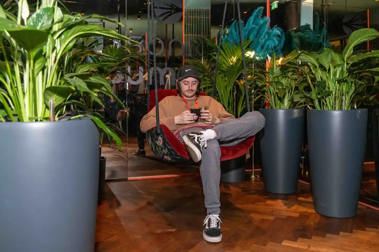 Mann sitzt entspannt in rotem Sessel zwischen Pflanzen auf Veranstaltung, hält Smartphone - Eventfotografie Wien