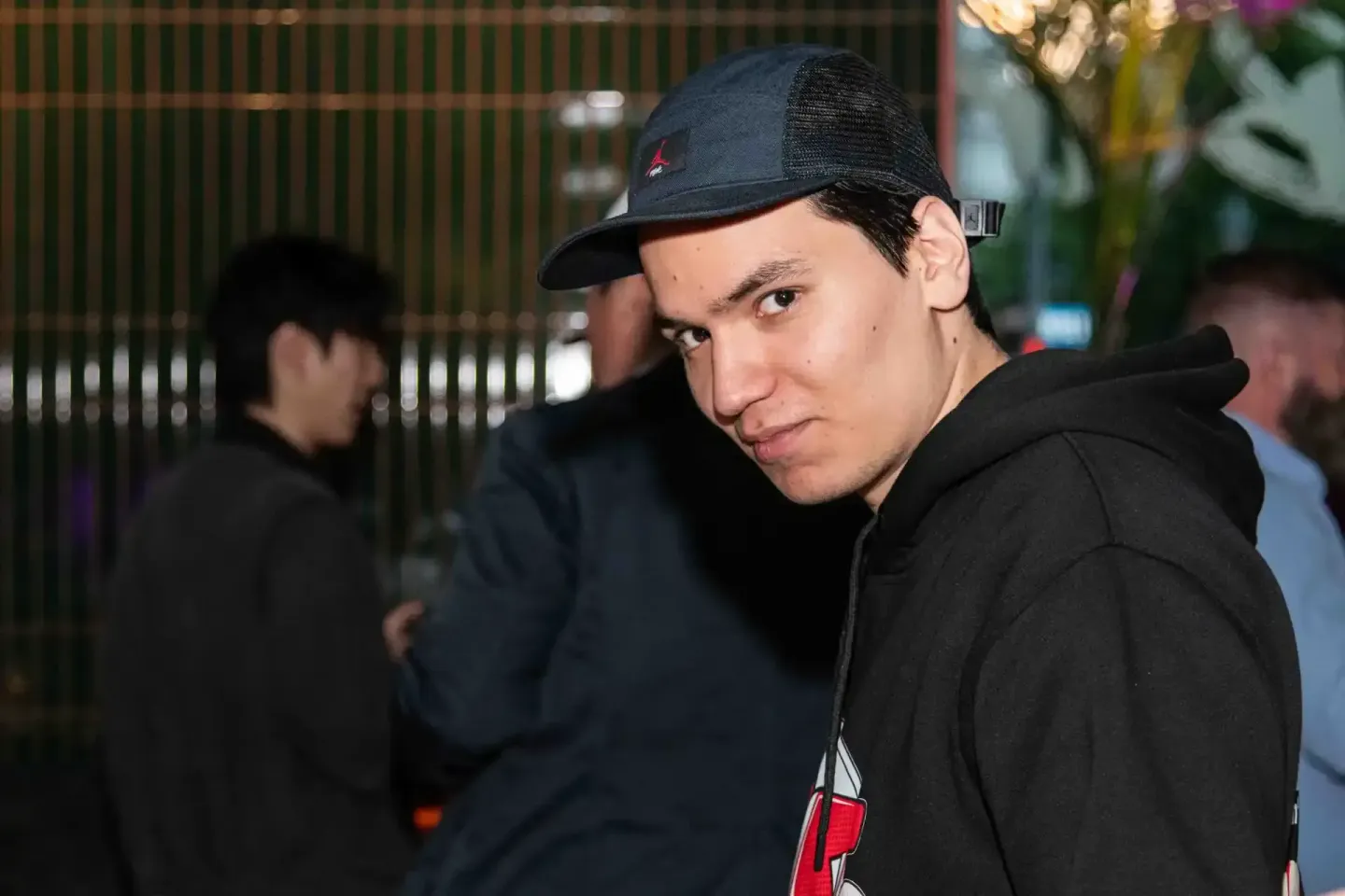 Besucher beim Sonic Summit Event in Wien - Eventfotografie eines jungen Mannes mit Kappe vor grünem Zaun