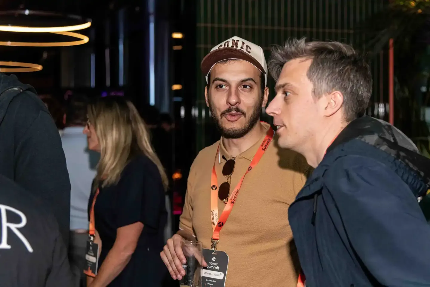 Zwei Männer im Gespräch beim Sonic Summit Event in Wien, einer trägt eine Kappe und ein rotes Lanyardband, Eventfotografie Wi
