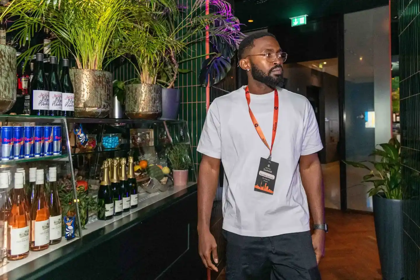 Mann mit Brille und Eventpass an stilvoller Bar mit Weinflaschen und Pflanzen beim Sonic Summit Wien