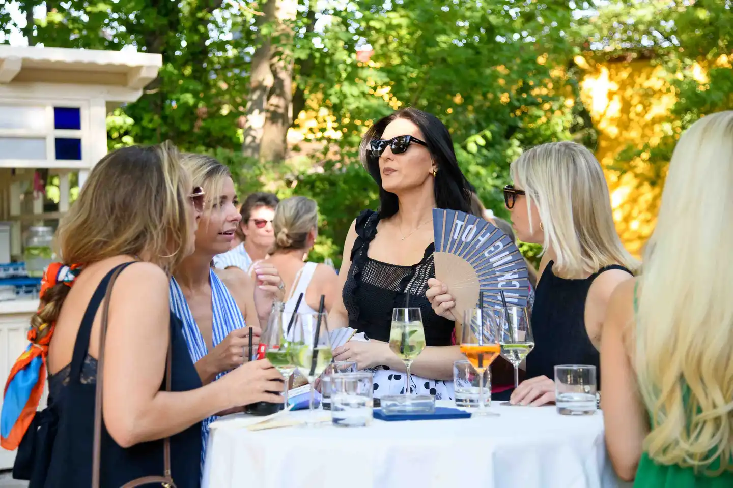 Kolleginnen am Stehtisch mit bedrucktem Fächer, Hugo und Aperol Spritz beim Firmensommerfest in Wien