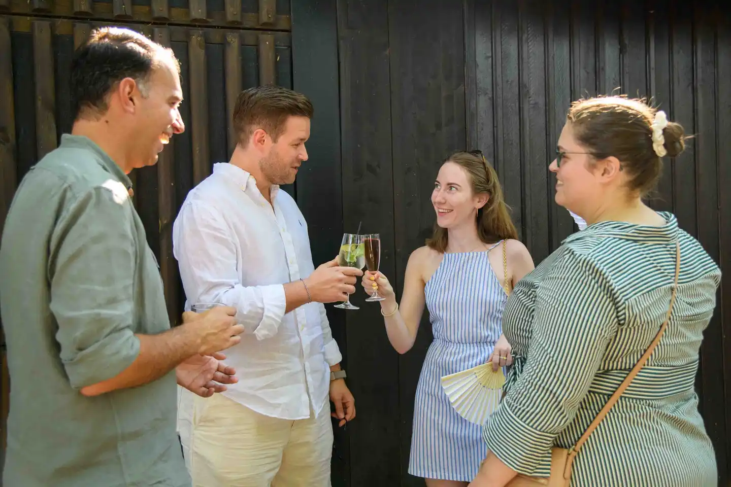 Vier Kollegen stoßen mit Hugo und Spritzer vor dunkler Holzwand an – Firmensommerfest in Wien