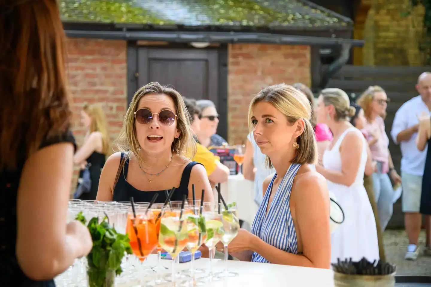 Zwei Kolleginnen an der Bar, davor Reihen vorbereiteter Spritzer-Gläser – Sommerfest Wien