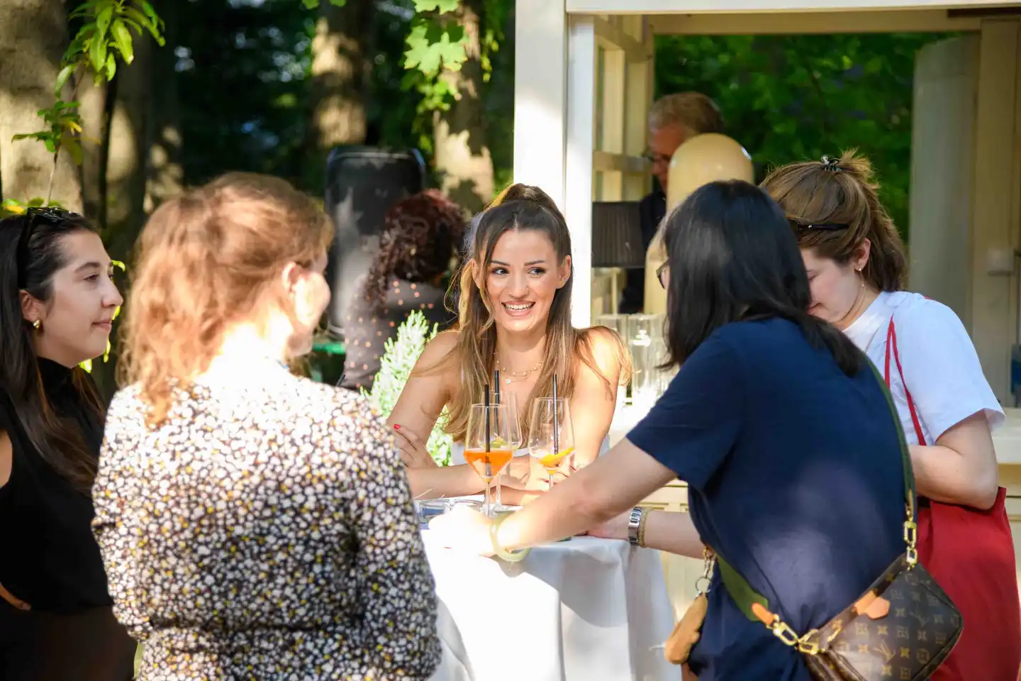 Lächelnde Mitarbeiterin am Stehtisch mit zwei Aperol Spritz im Abendlicht – Sommerfest Wien