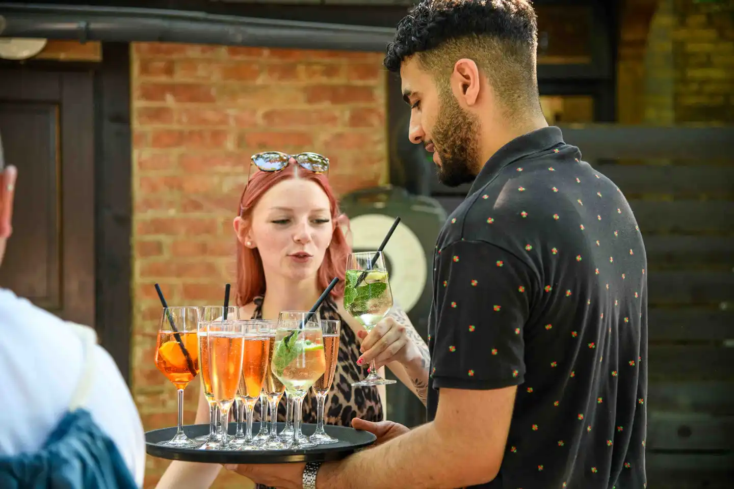 Junge Mitarbeiterin nimmt einen Hugo vom Aperitif-Tablett vor der Ziegelwand – Eventfotografie Wien Sommerfest