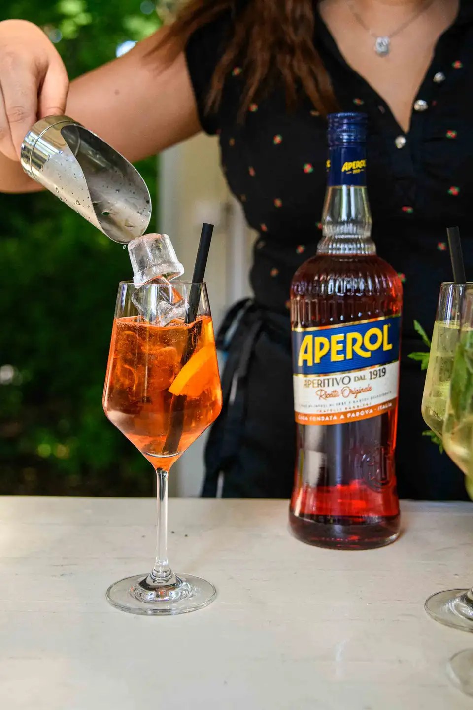 Barfrau gibt Eiswürfel in ein Glas Aperol Spritz, daneben die Aperol-Flasche – Sommerfest in Wien