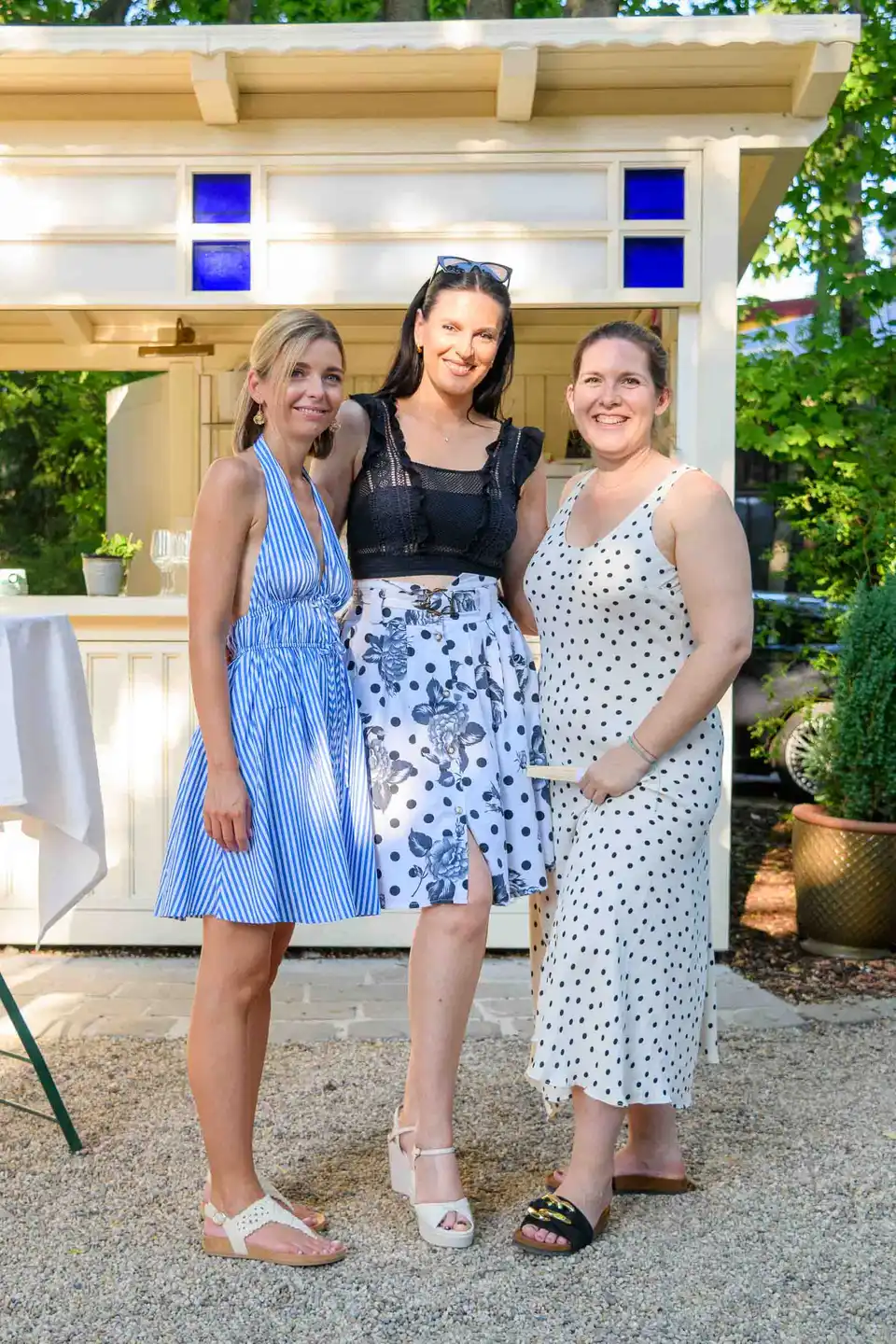 Drei Kolleginnen in Sommerkleidern stehen vor dem weißen Gartenpavillon – Firmensommerfest Wien