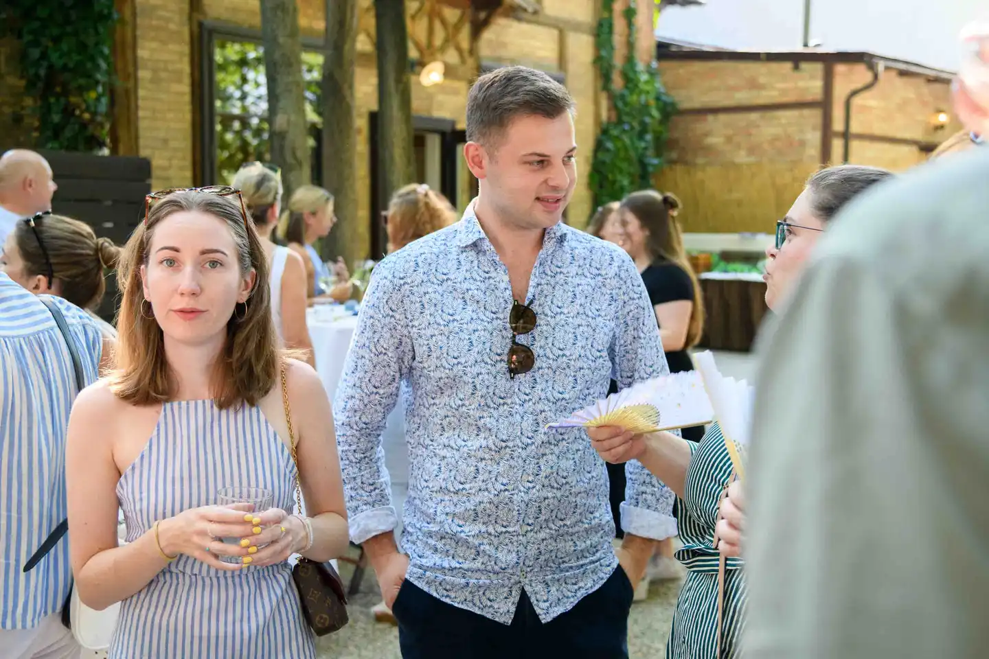 Gäste im Innenhof mit Fächern und Wassergläsern vor der Ziegelfassade – Sommerfest Eventfotografie Wien