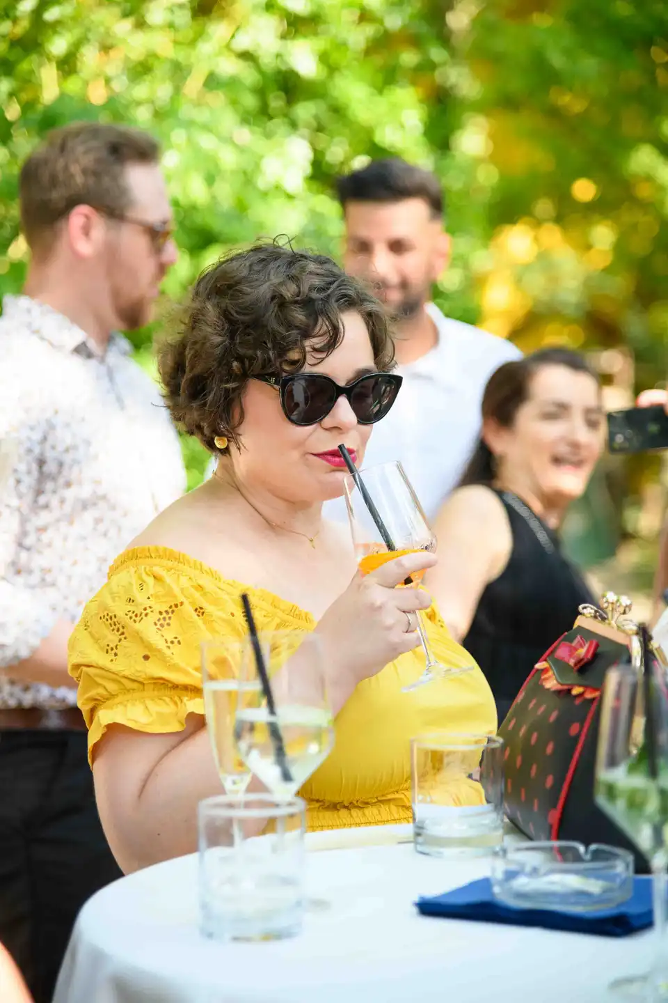 Gast im gelben Sommerkleid trinkt einen Spritzer mit Strohhalm am Stehtisch – Sommerfest Eventfotografie Wien