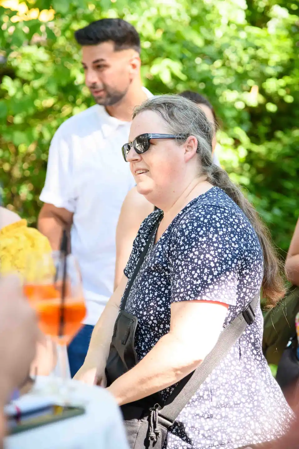Mitarbeiterin mit Sonnenbrille und langem Zopf im geblümten Top beim Stehempfang – Sommerfest Wien