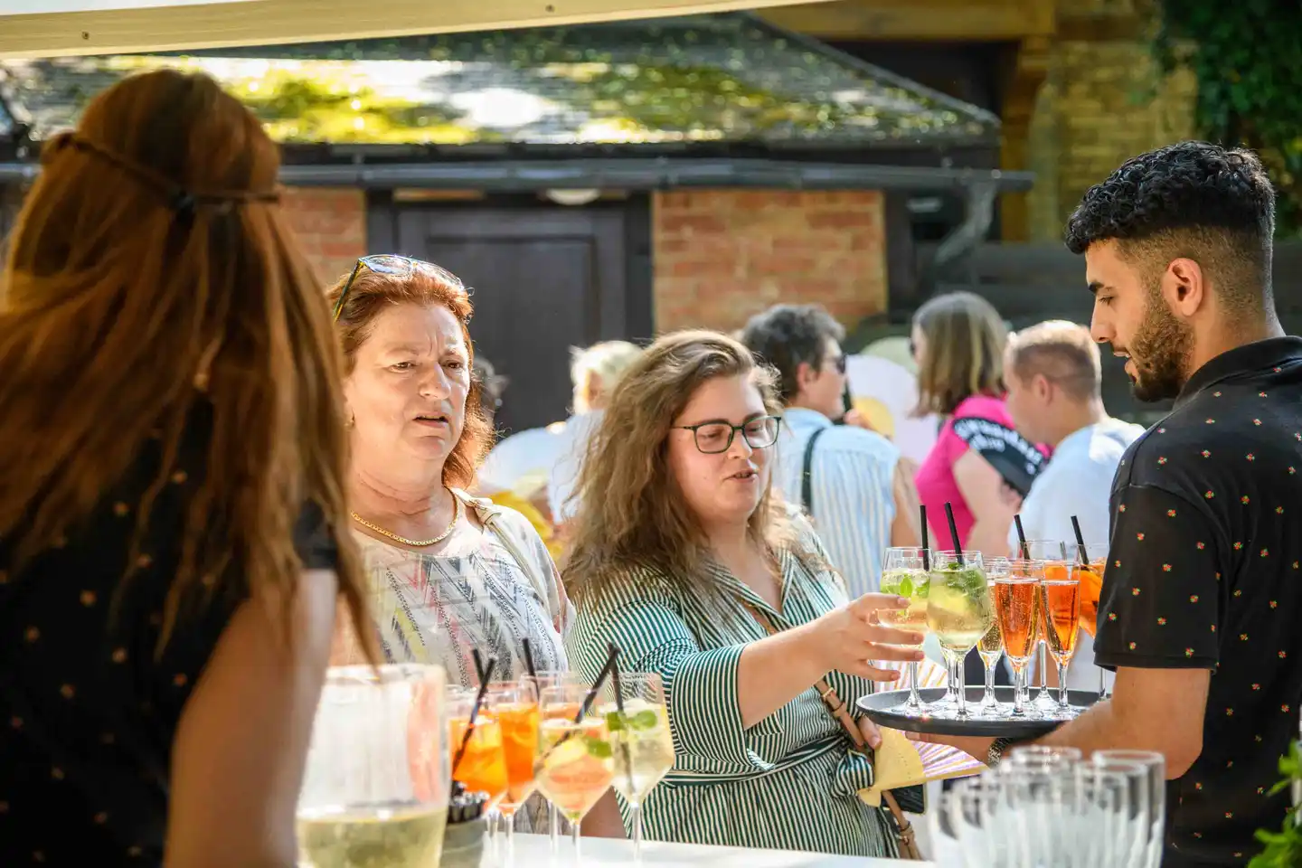 Gast nimmt einen Hugo vom Tablett des Kellners, weitere Gäste warten am Stehtisch – Eventfotografie Wien