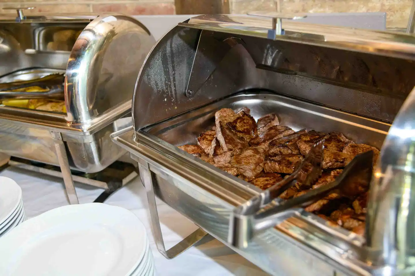 Chafing Dish mit gegrilltem Fleisch und Tellerstapel am Buffet des Firmensommerfests in Wien