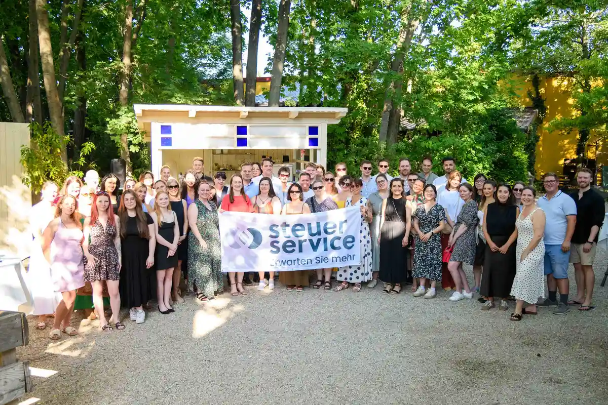Gruppenfoto des gesamten Teams mit Steuer & Service Banner im Gastgarten – Sommerfest Eventfotografie Wien