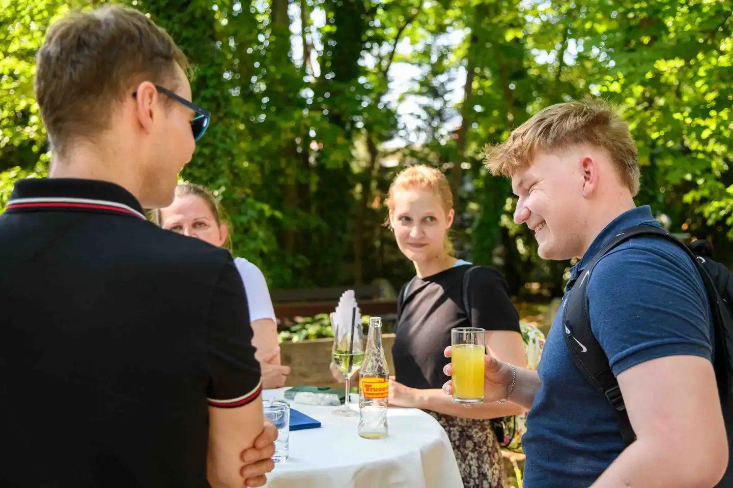 Junger Mitarbeiter mit Orangensaft im Gespräch mit Kollegen am Stehtisch – Sommerfest Eventfotografie Wien