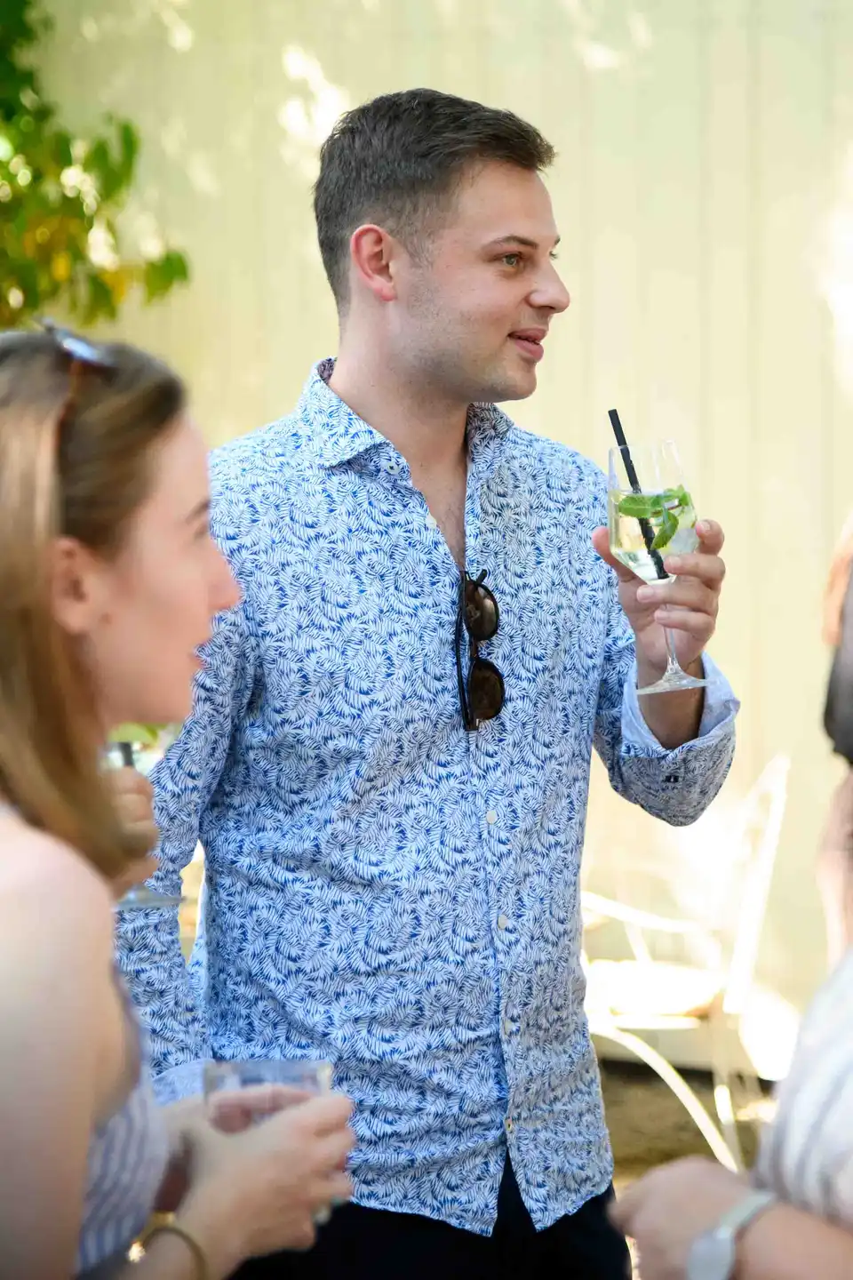 Kollege im blau gemusterten Hemd hält einen Hugo und erzählt in der Runde – Sommerfest Eventfotografie Wien