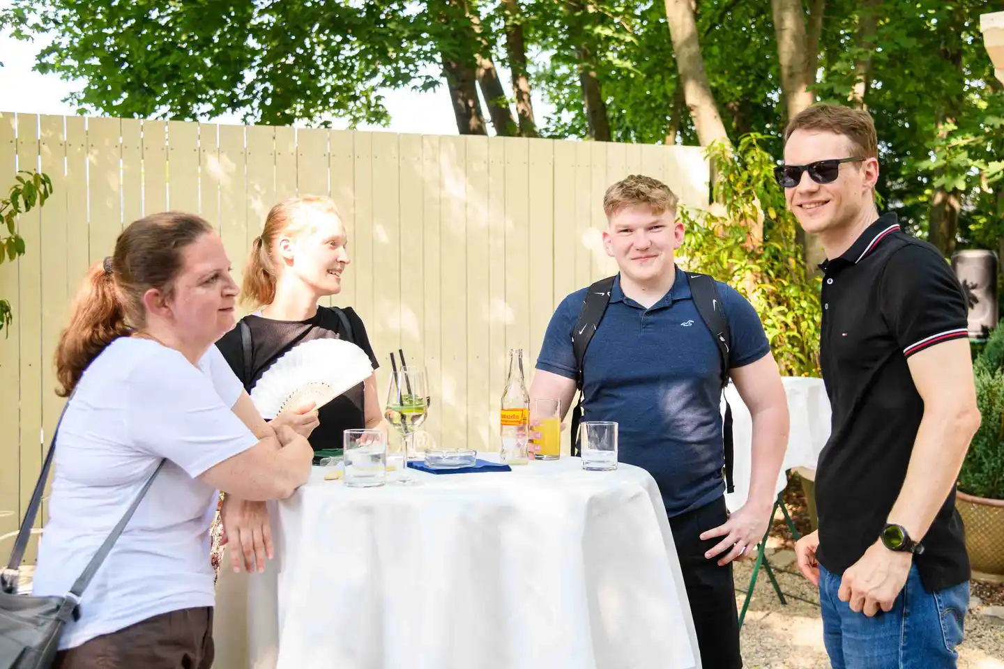 Zwei Kollegen im Polo posieren am Stehtisch neben zwei Kolleginnen, Almdudler am Tisch – Sommerfest Wien