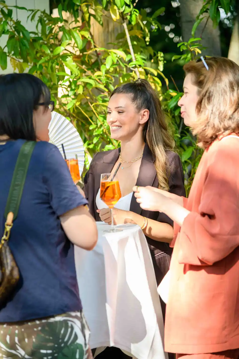 Kollegin im braunen Blazer hält einen Aperol Spritz und lächelt am Stehtisch – Sommerfest Eventfotografie Wien