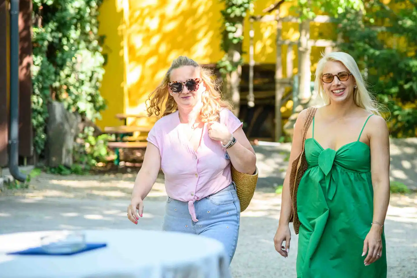 Zwei Kolleginnen gehen lachend über den Kiesweg vor gelber Hauswand zum Fest – Sommerfest Eventfotografie Wien
