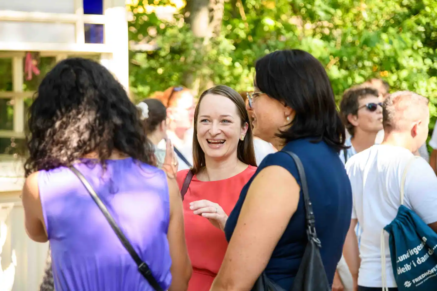 Mitarbeiterin im roten Kleid lacht im Gespräch mit zwei Kolleginnen im Gastgarten – Sommerfest Eventfotografie Wien