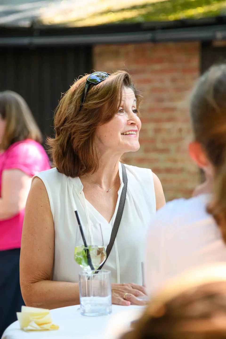 Gast in weißer Bluse lächelt beim Gespräch am Stehtisch, Hugo im Glas – Sommerfest Eventfotografie Wien