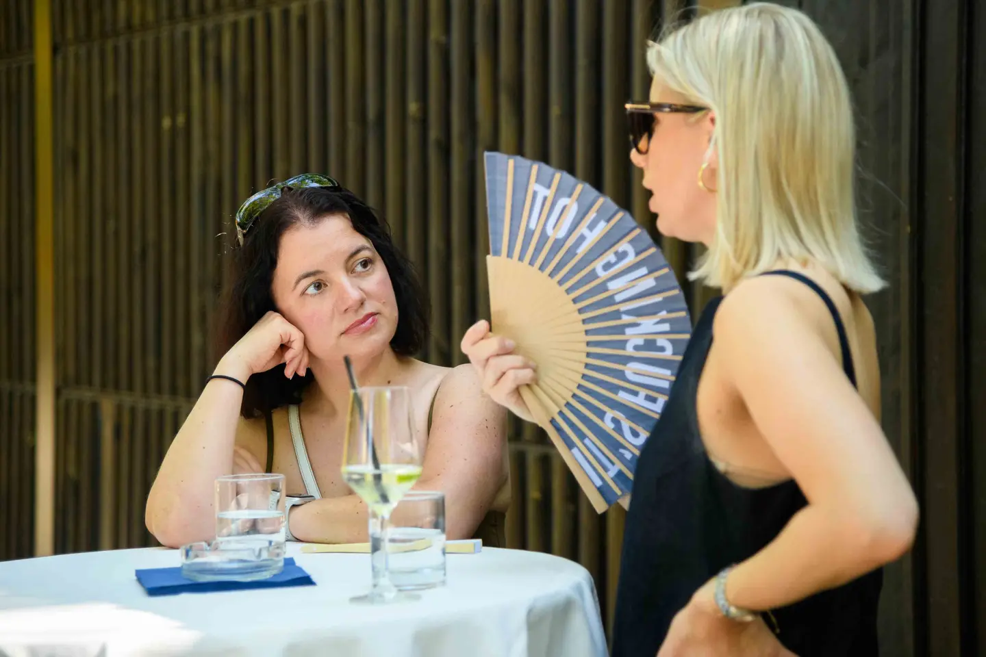Zwei Kolleginnen am Stehtisch im Schatten, eine hält einen bedruckten Fächer – Sommerfest Eventfotografie Wien