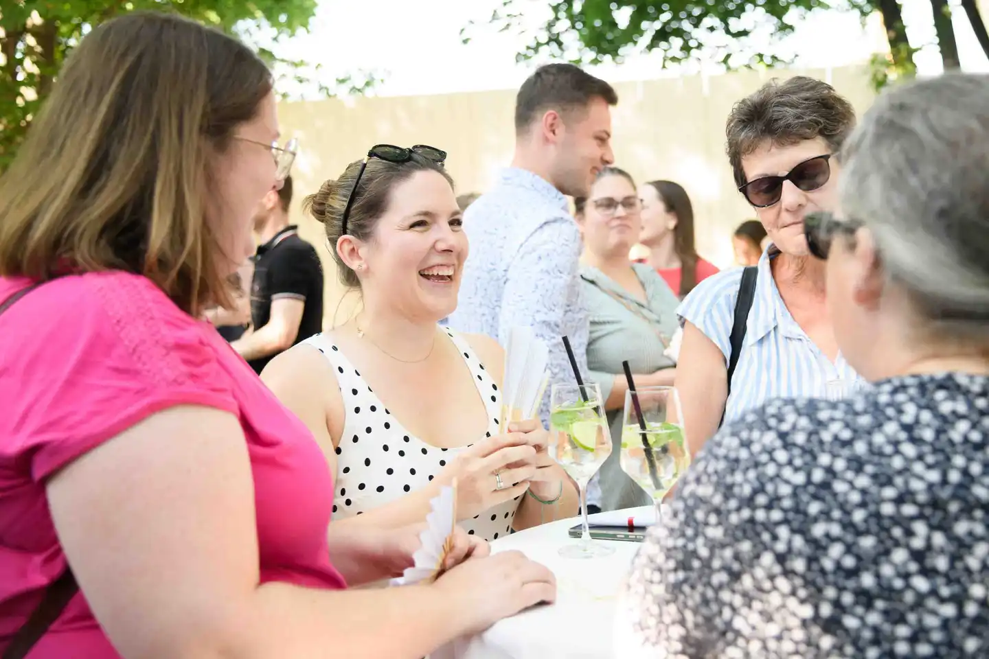 Plaudernde Runde am Stehtisch mit Fächern und Weißweinspritzern im Gastgarten – Sommerfest Wien