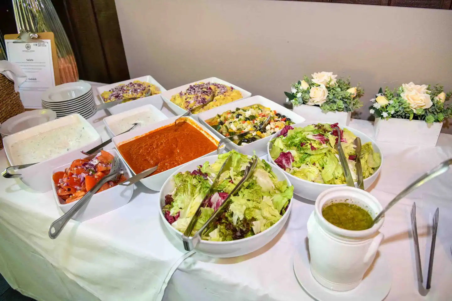 Salatbuffet mit Blattsalaten, Aufstrichen und Dressing auf weißer Tischdecke – Firmensommerfest Wien