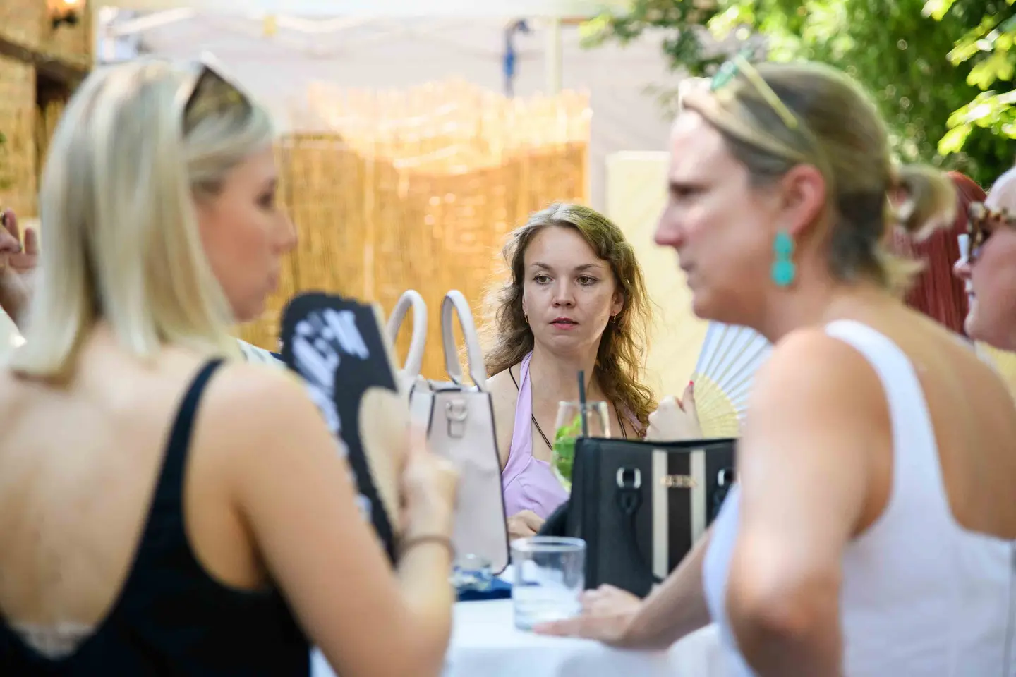 Stehtischgespräch mit bedrucktem und weißem Fächer, Handtaschen auf dem Tisch – Sommerfest Wien
