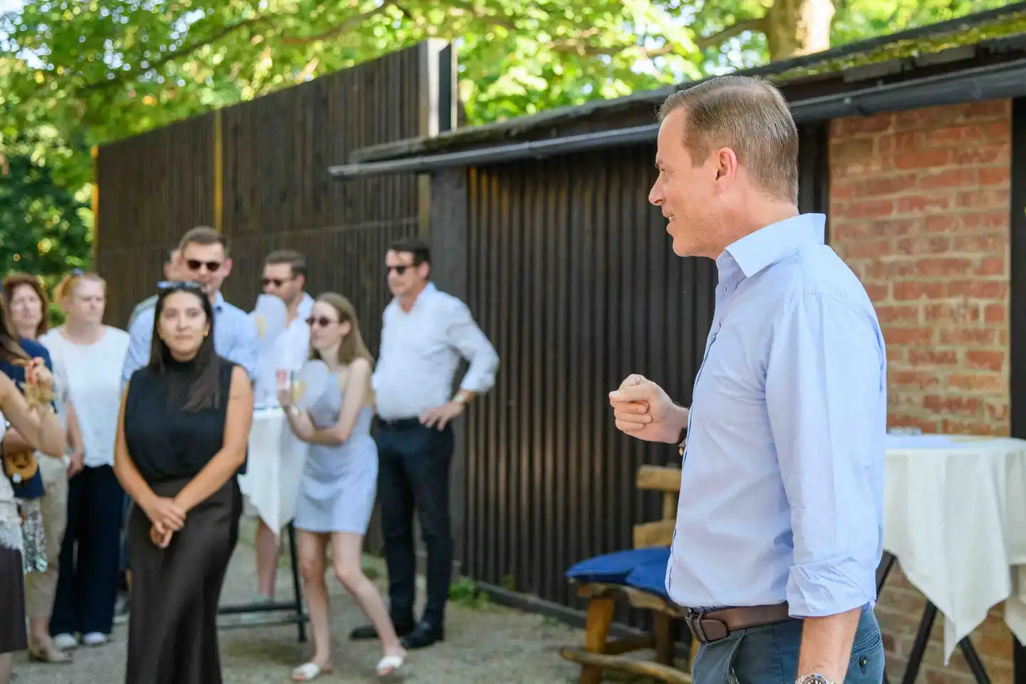 Mitarbeiterinnen und Mitarbeiter hören der Ansprache des Chefs im Gastgarten zu – Sommerfest Wien