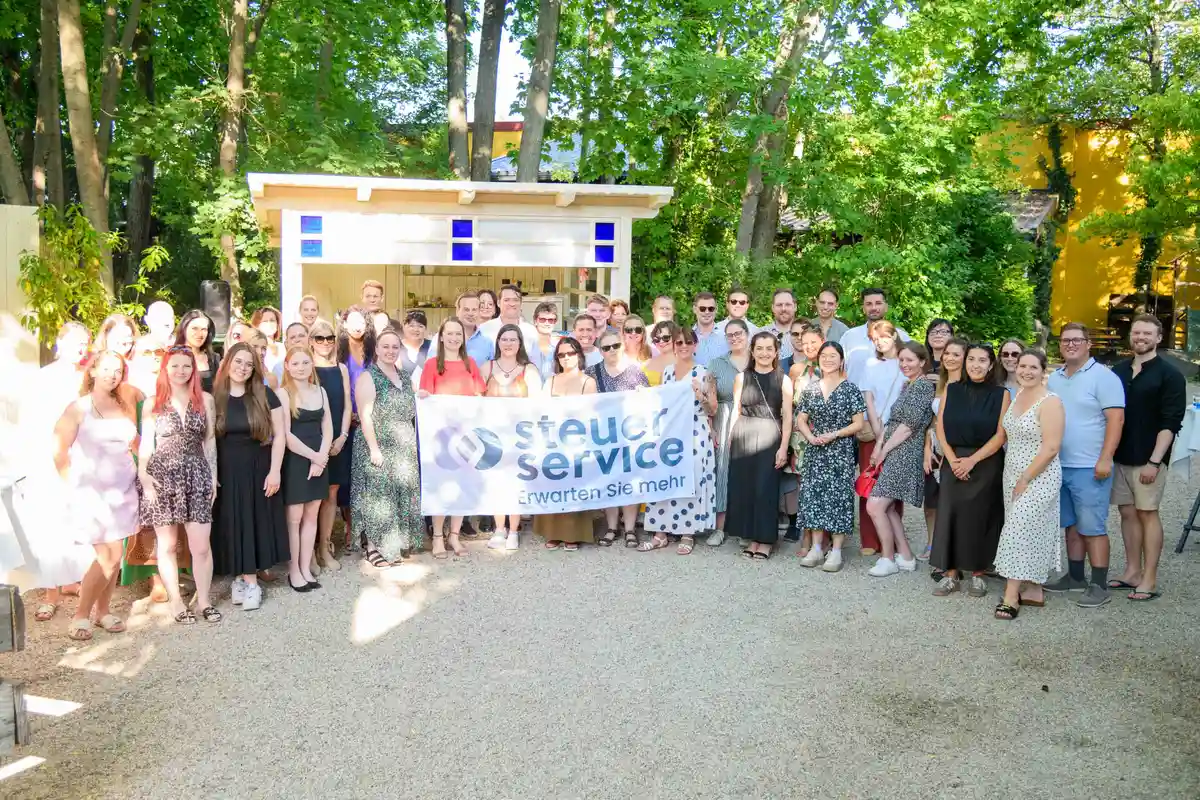 Weite Aufnahme des Teamfotos mit Firmenbanner vor der weißen Gartenbar – Sommerfest Eventfotografie Wien