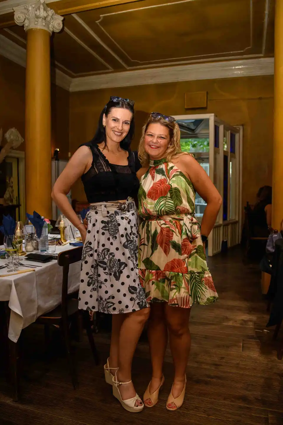 Zwei Kolleginnen posieren Arm in Arm im gelben Restaurantsaal beim Sommerfest in Wien