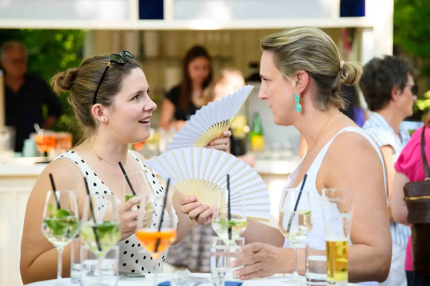 Zwei Kolleginnen mit weißen Fächern im Gespräch an der Gartenbar – Sommerfest Eventfotografie Wien