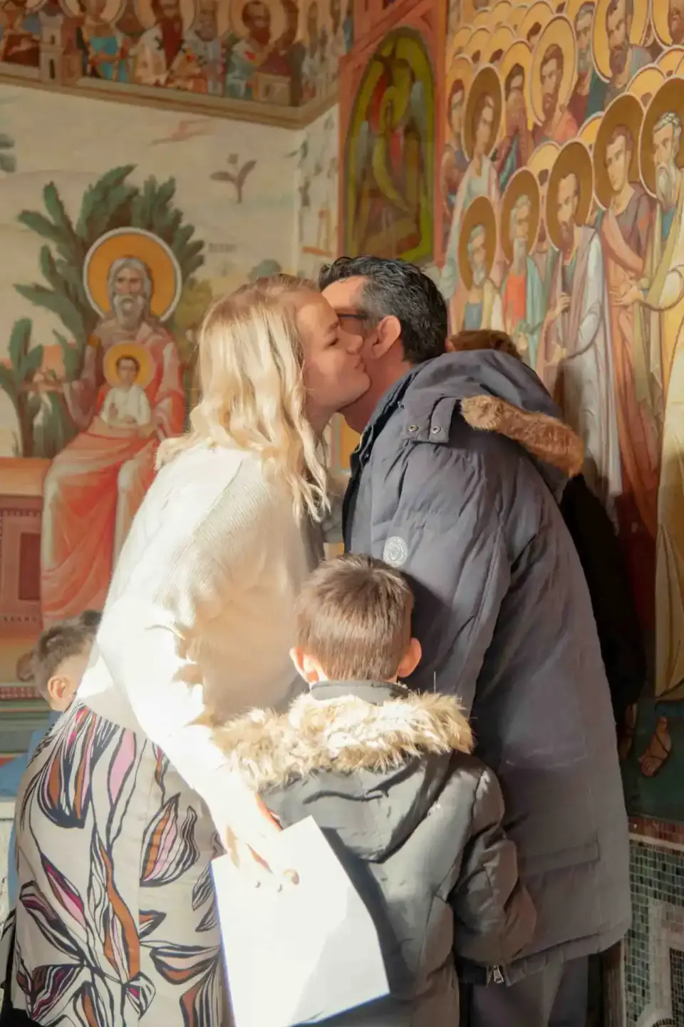 Familie mit zwei Kindern küsst sich vor religiösen Ikonen bei einer Taufe - Eventfotograf Wien dokumentiert den Moment