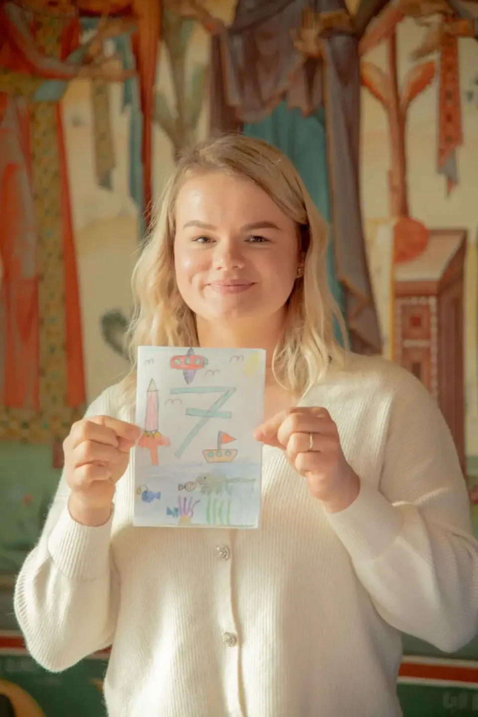 Mädchen hält stolz ihre bunte Kinderzeichnung mit Rakete und Boot in die Kamera – professionelle Eventfotografie Wien