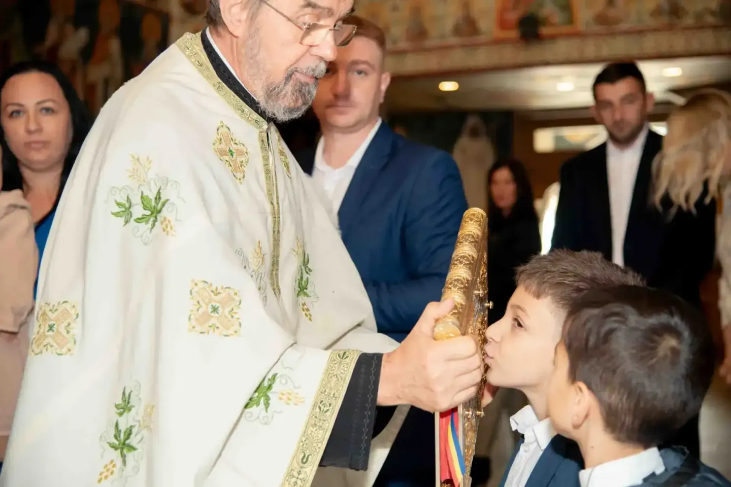 Priester in weißem Ornatsgewand führt Taufzeremonie mit zwei Kindern durch, Eventfotograf Wien dokumentiert religiöse Feier