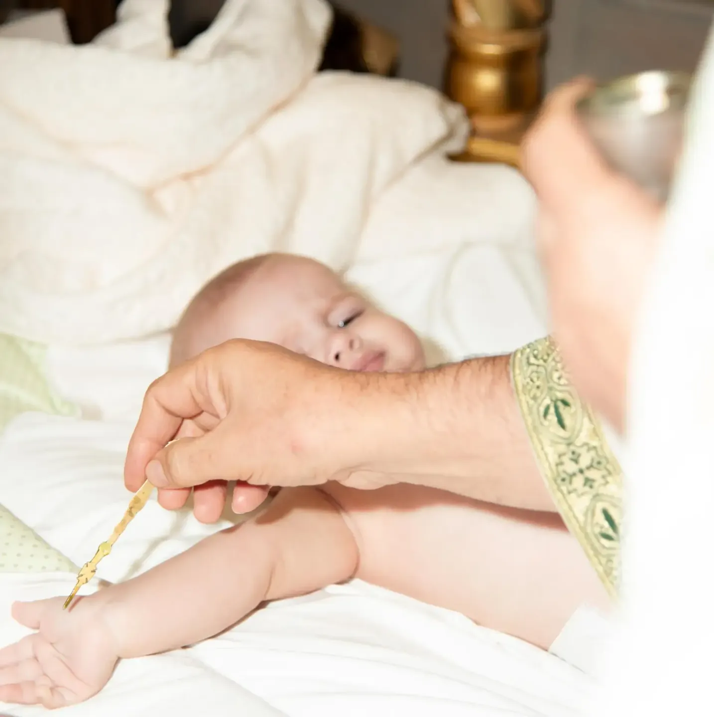 Taufe Wien: Ein Priester segnet ein schlafendes Neugeborenes mit Weihwasser während der Taufzeremonie