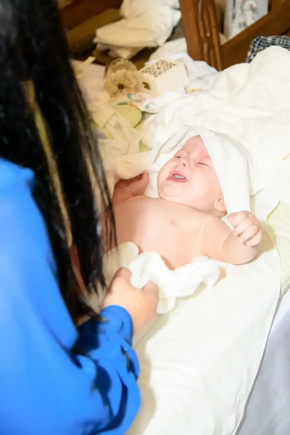 Eventfotograf Wien dokumentiert zarte Momente bei einer Taufe: Ein neugeborenes Baby in weißen Tüchern wird von einer Person 