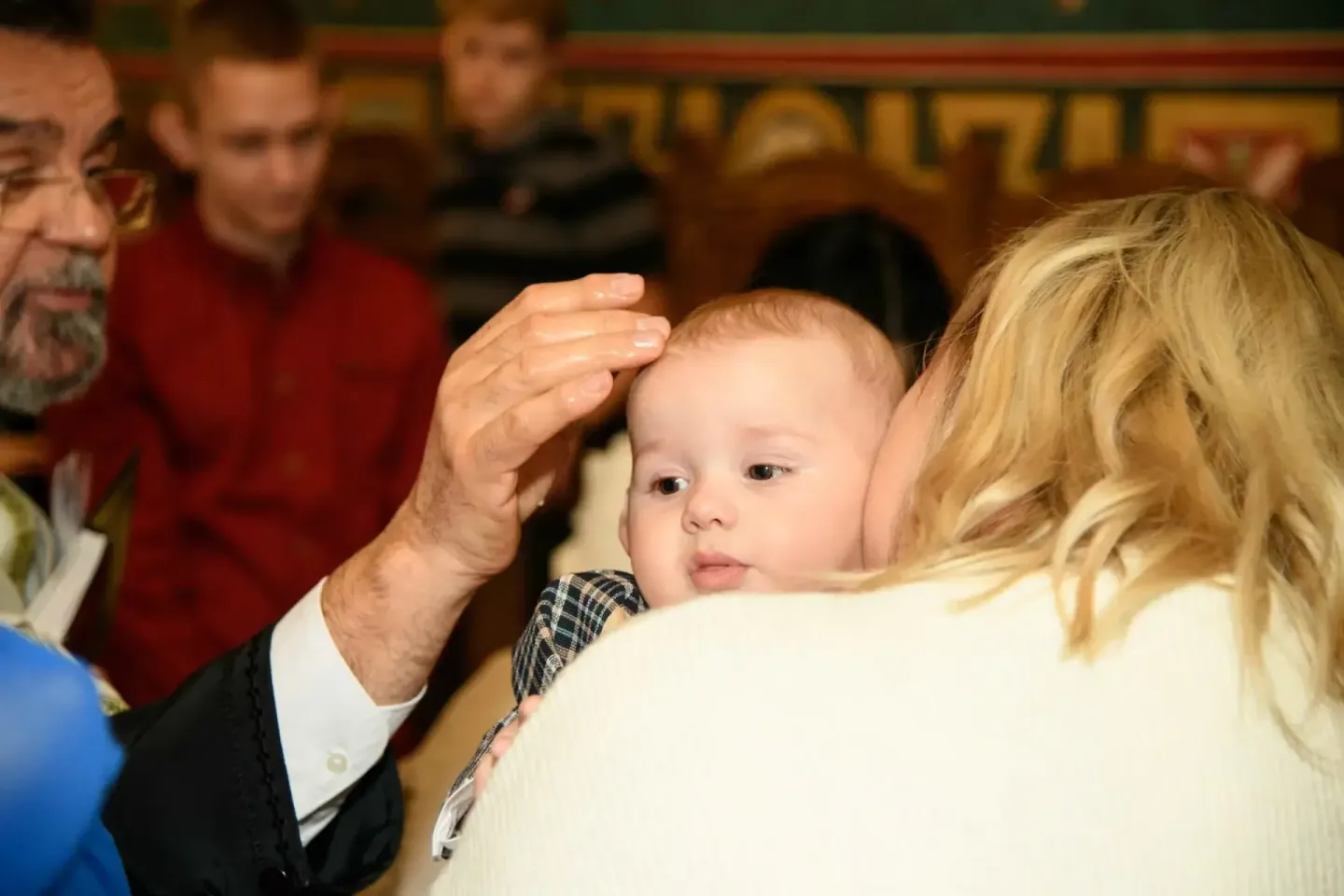 Taufe Wien: Priester segnet Baby während Eltern und Gäste zuschauen, professionelle Eventfotografie