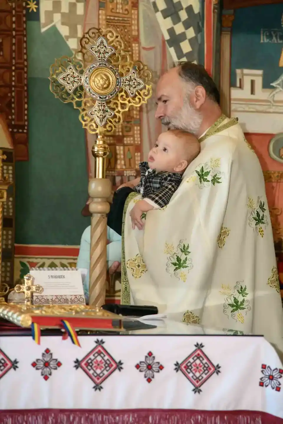 Priester hält Säugling während Taufezeremonie in einer Kirche mit goldenem Kreuz und orthodoxer Dekoration - Eventfotograf Wi
