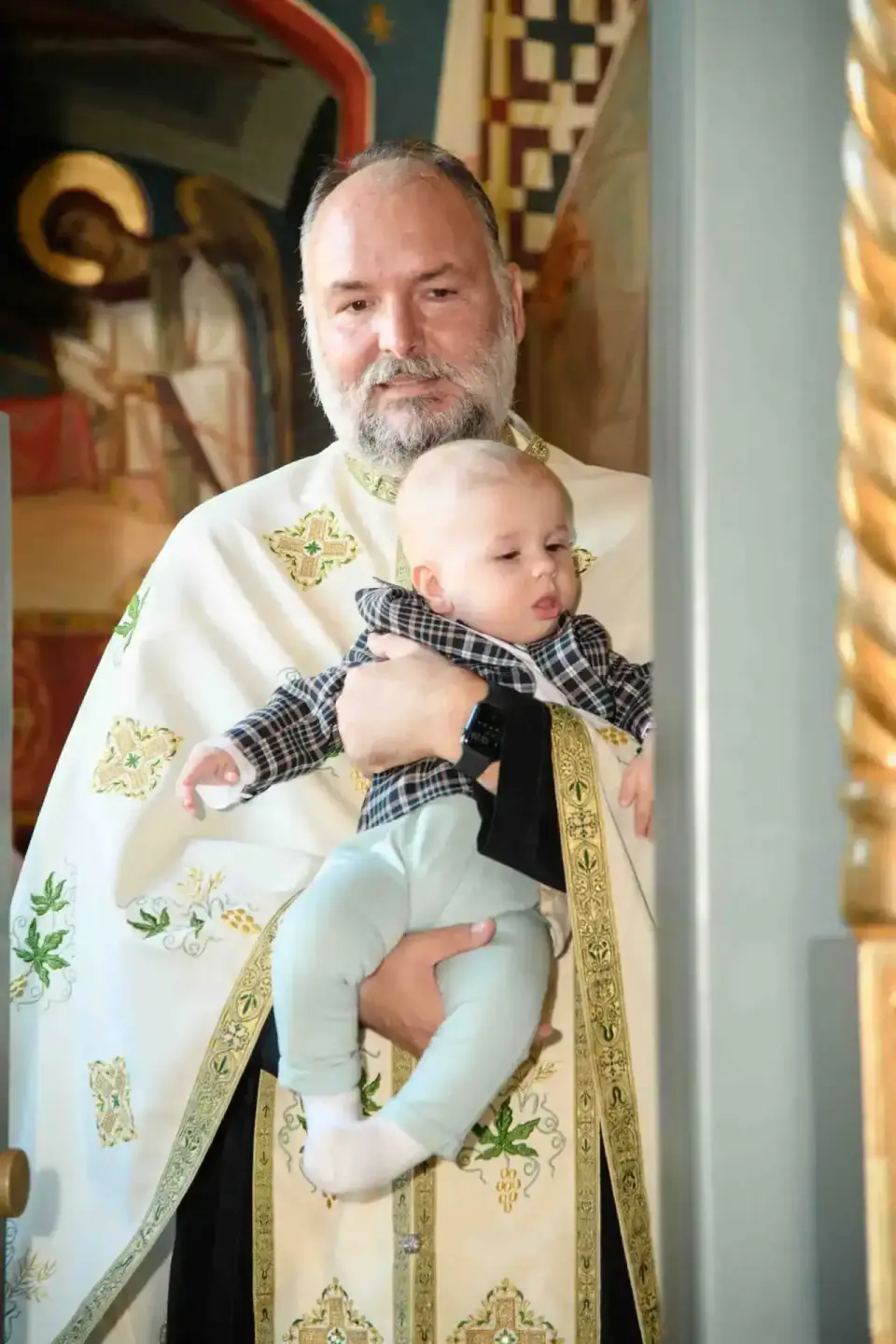 Priester in weißem Messgewand hält Neugeborenes während Taufe in Wiener Kirche - Eventfotografie Wien