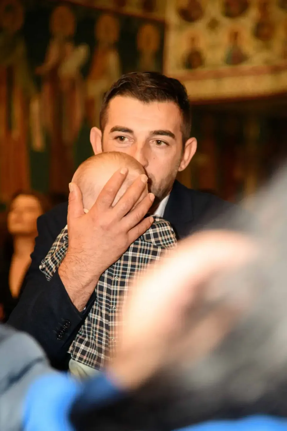 Mann in Anzug hält Baby während Tauffeier - Eventfotografie Wien