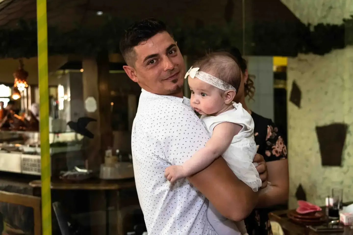 Vater hält lächelnd sein Baby mit Stirnband bei einer Taufe – professionelle Eventfotografie Wien