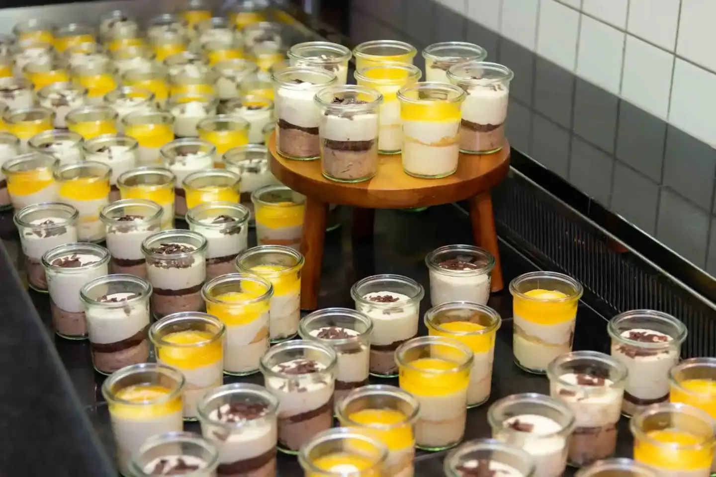 Elegante Desserts in Gläsern bei einem Firmenevent Wien - mehrschichtige Kreationen mit Schokolade, Creme und gelbem Topping 