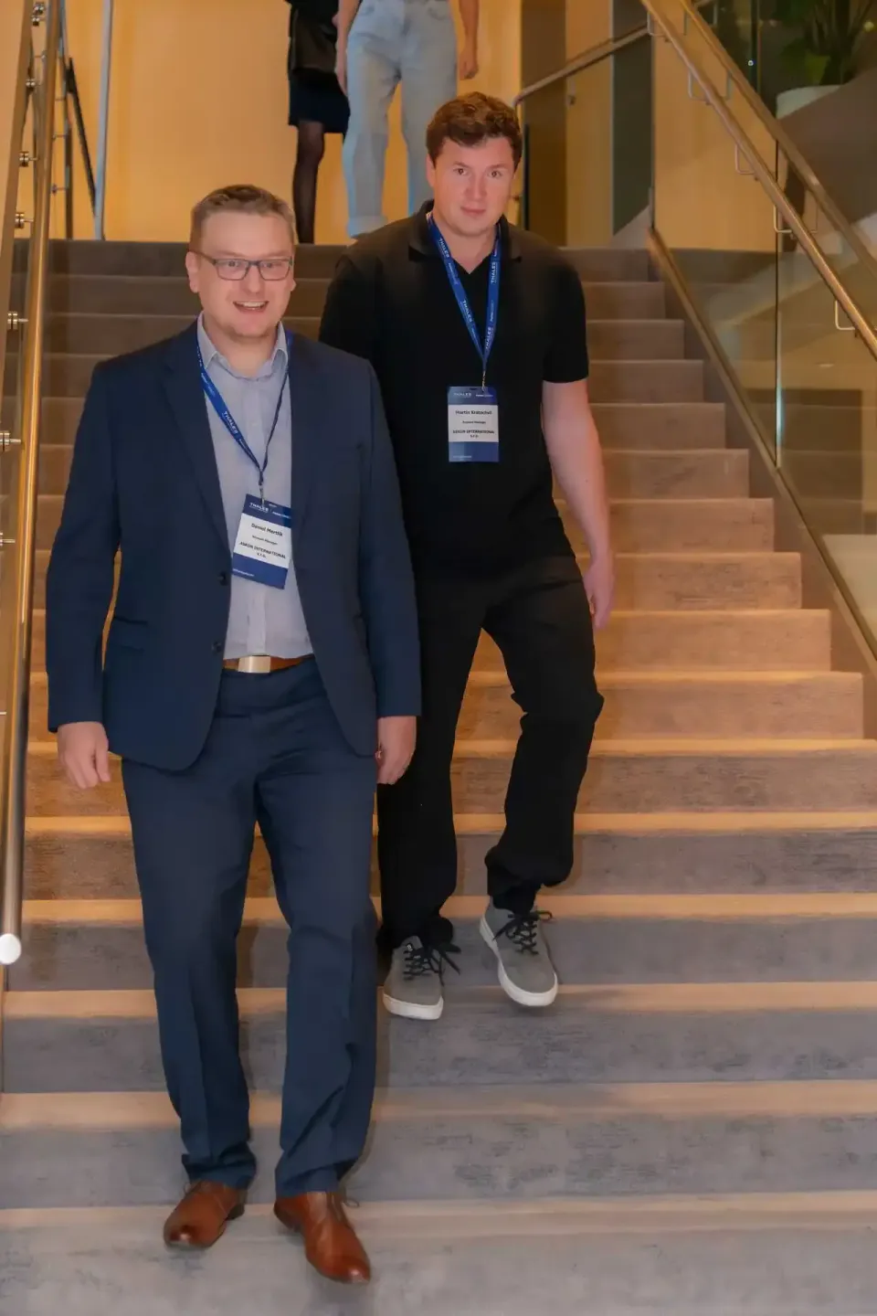 Zwei junge Männer mit Namensschildern gehen lächelnd eine Treppe hinunter auf einem Firmenevent in Wien
