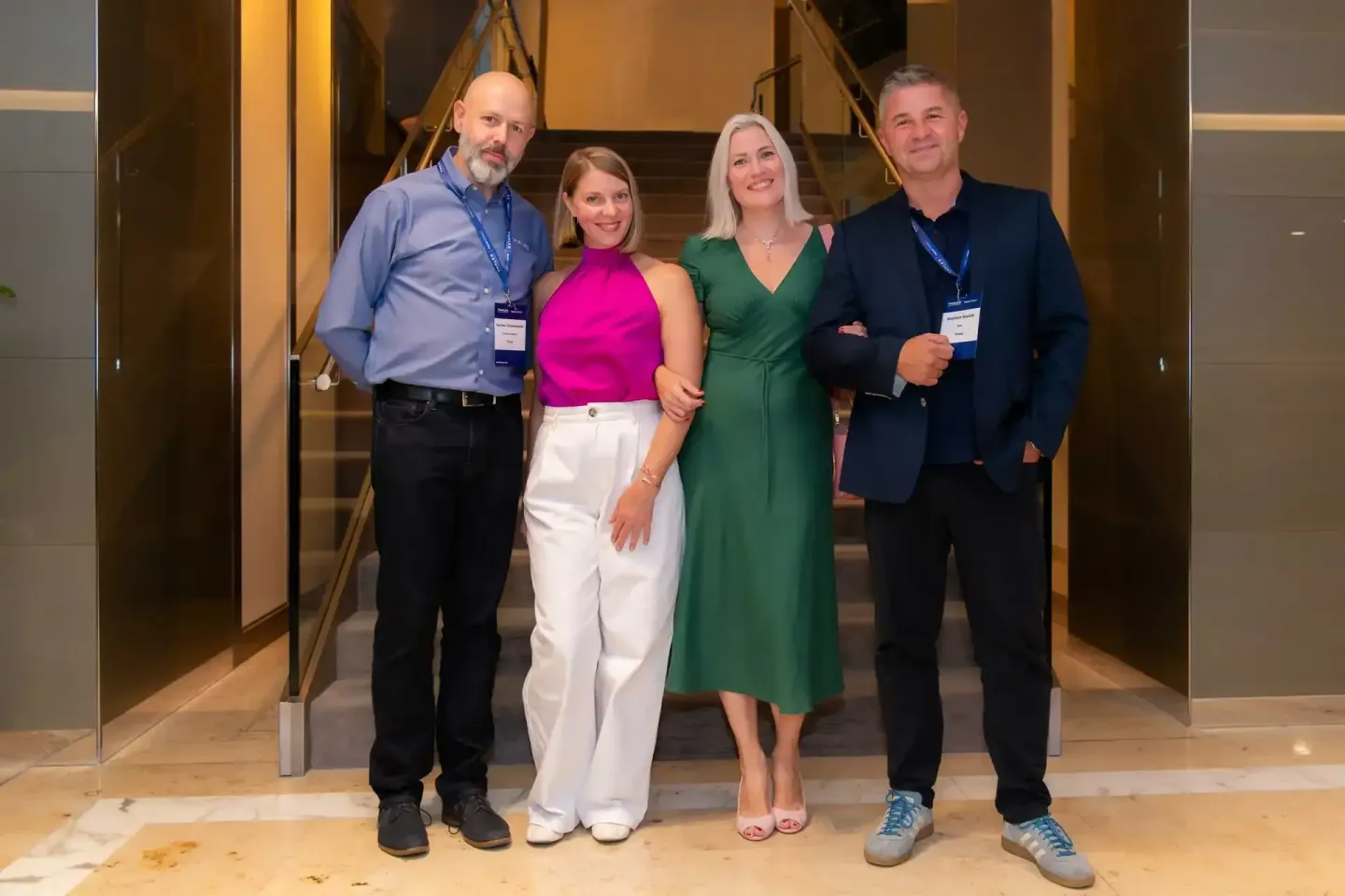 Vier Personen in eleganter Geschäftskleidung bei einem Firmenevent Wien, zwei tragen Namensschilder, vor moderner Glasarchite