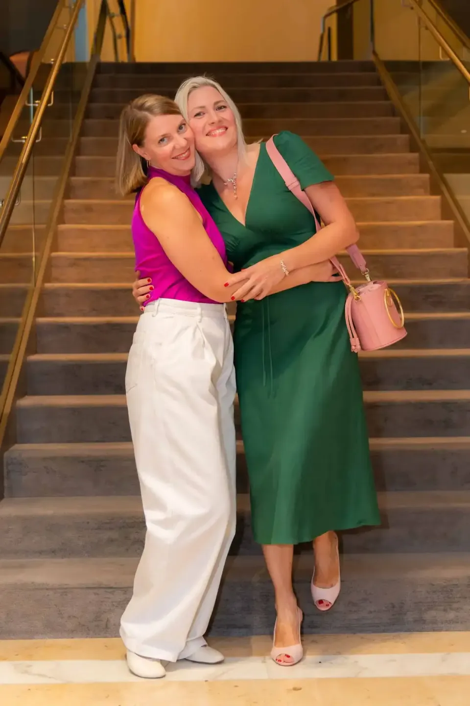 Zwei Frauen umarmen sich lachend auf einer Treppe bei einem Firmenevent Wien - Eventfotografie
