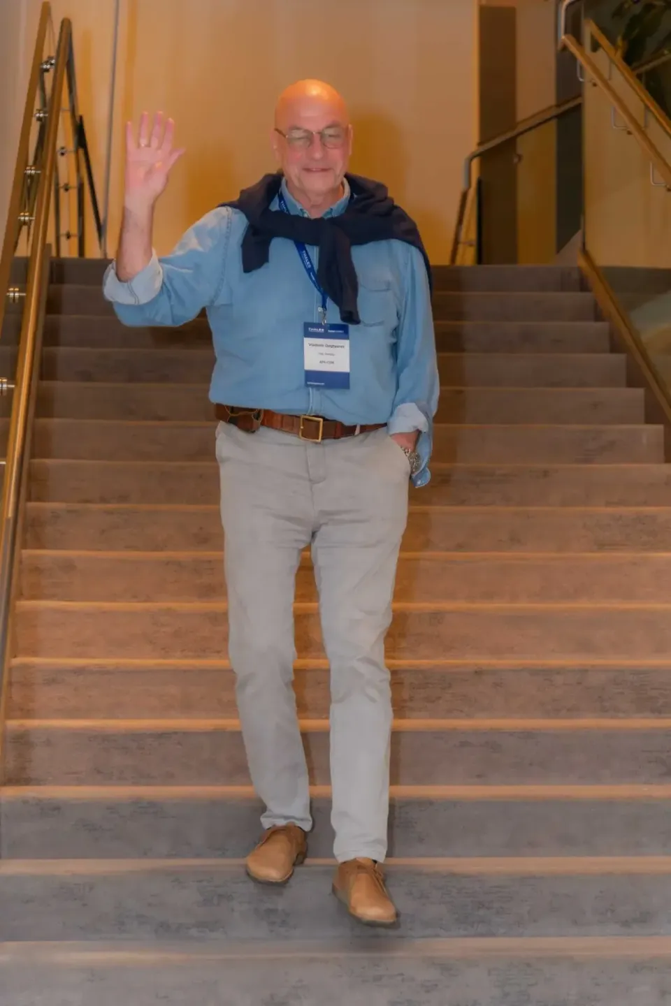 Mann mit Brille und Namensschild winkt auf einer Treppe - Eventfotografie Wien bei Thales Firmenevent